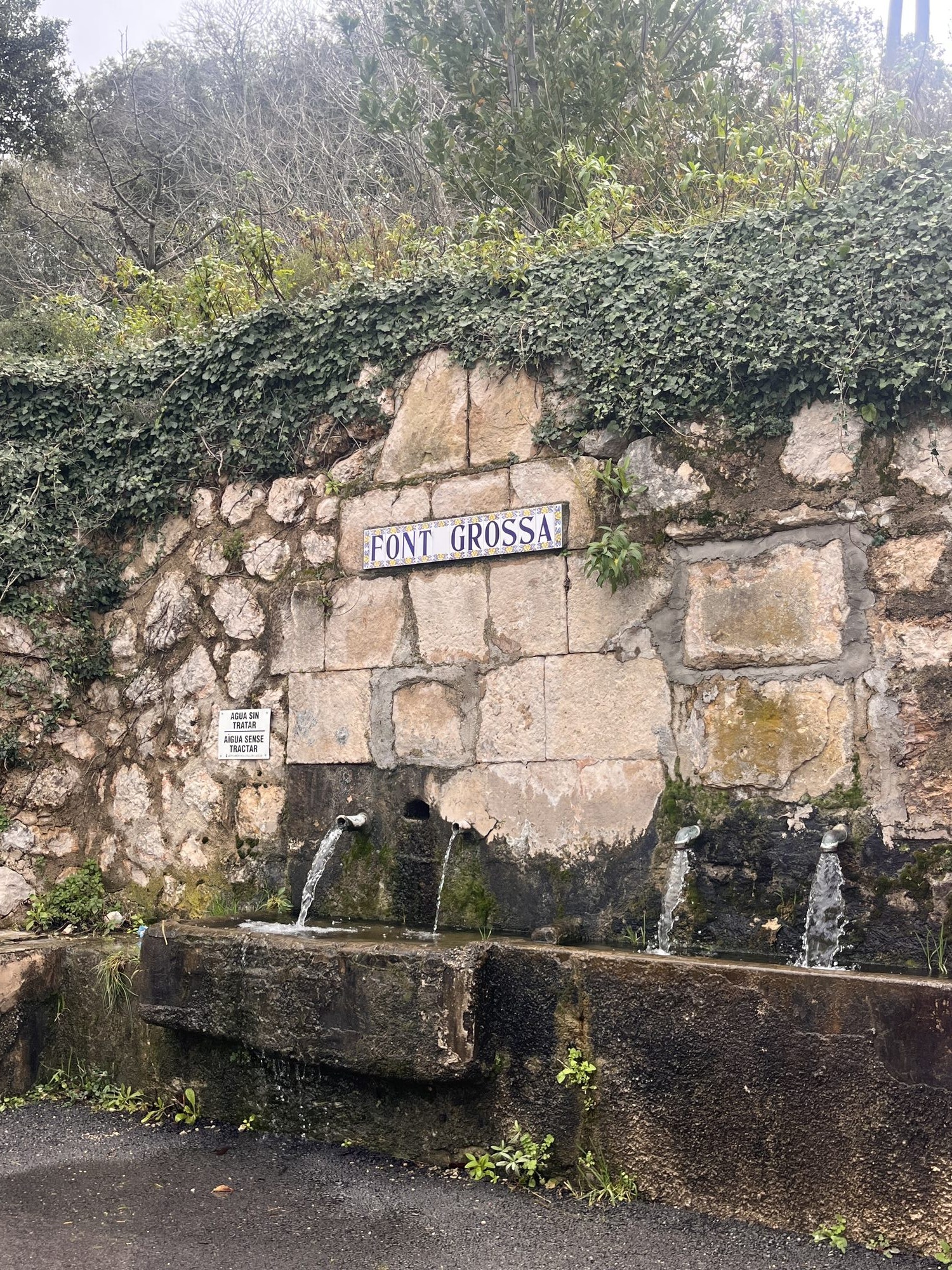 Rustic stone wall with water spouts and Font Grossa sign in Spain.